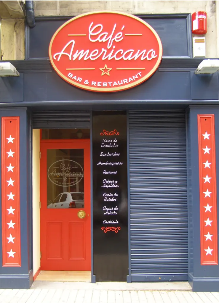 Fachada del Café Americano con rótulo circular y paneles laterales rojos