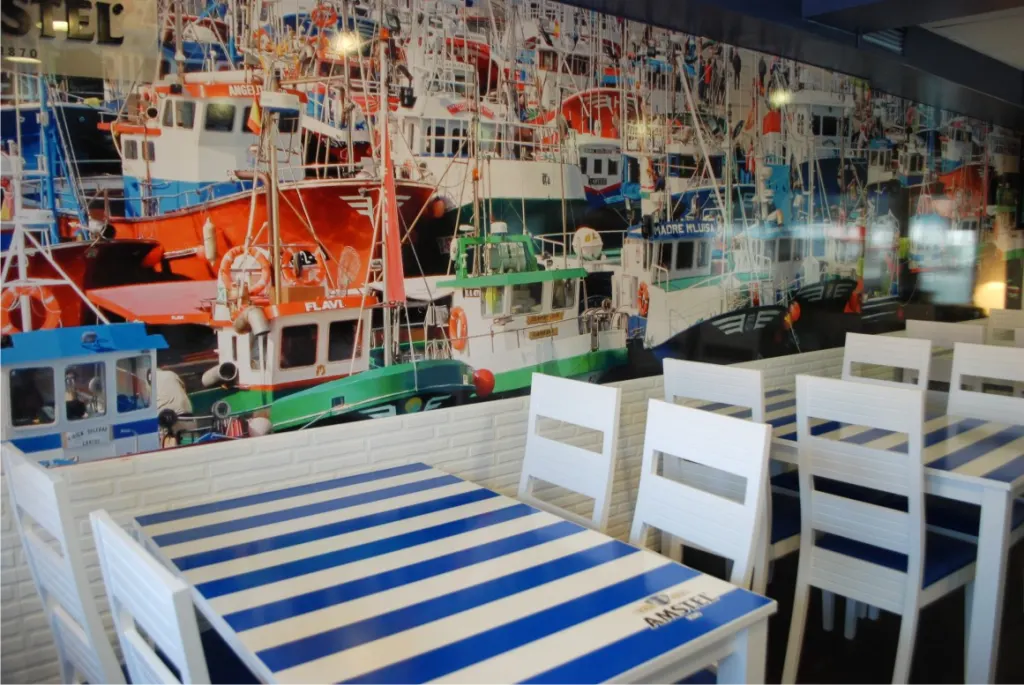 Restaurante con mural fotográfico de barcos pesqueros y mesas a rayas azules y blancas