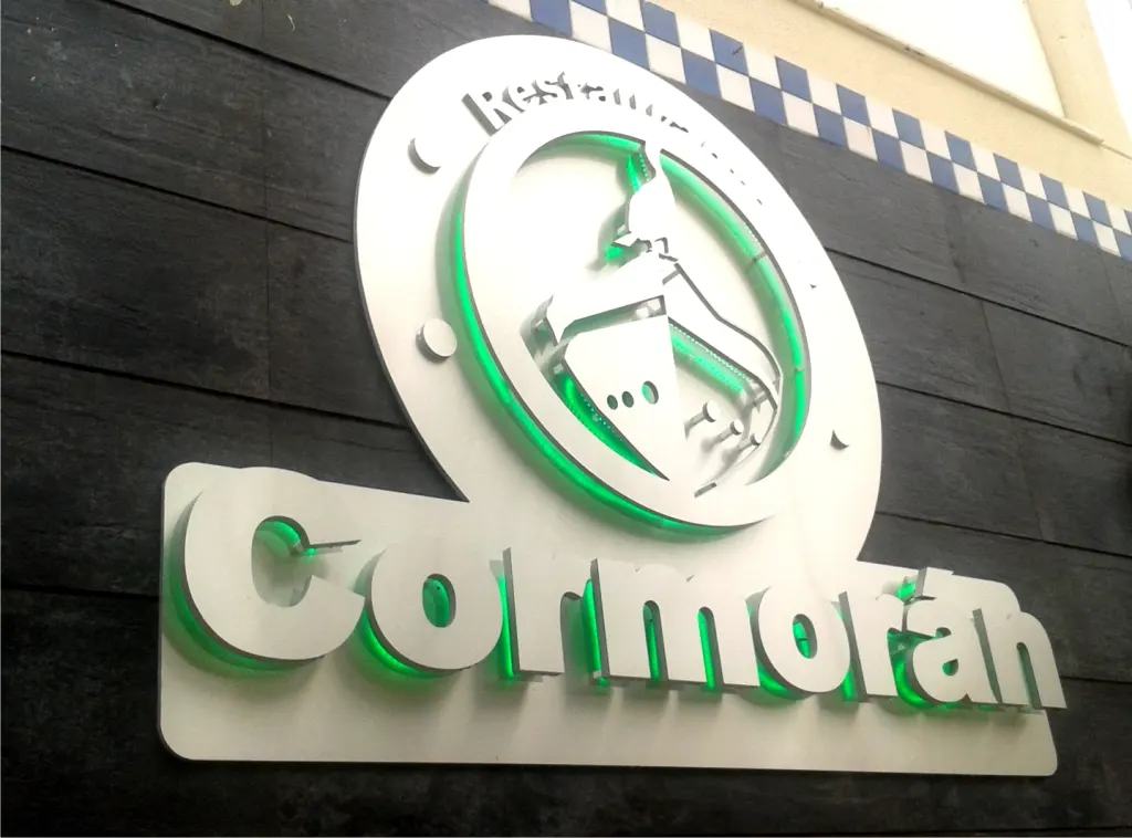 Rótulo corpóreo del restaurante Cormorán sobre una fachada de madera oscura