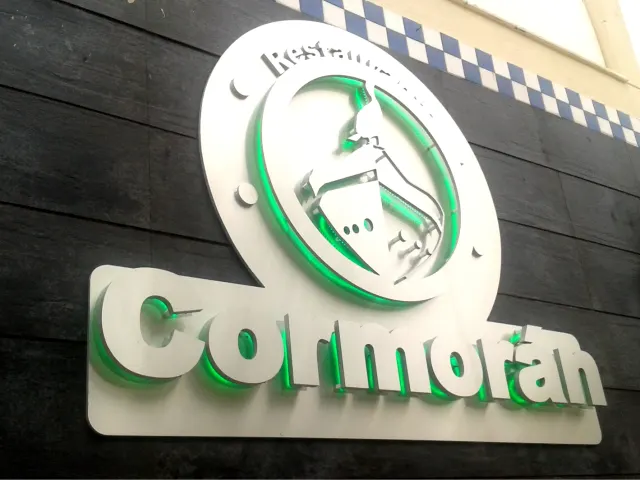 Rótulo corpóreo del restaurante Cormorán sobre una fachada de madera oscura