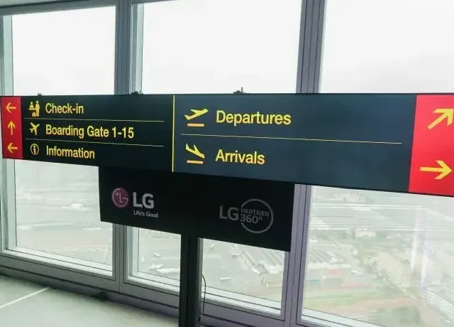 Señal direccional de aeropuerto con indicaciones de facturación, salidas y llegadas