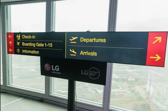 Señal direccional de aeropuerto con indicaciones de facturación, salidas y llegadas