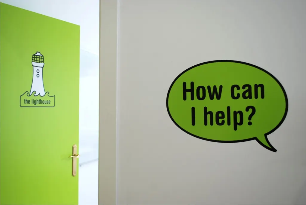 Vinilos en pared y puerta con un bocadillo «How can I help?» y el logotipo de un faro